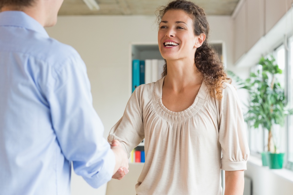Young businesswoman shaking hands with male colleague in office